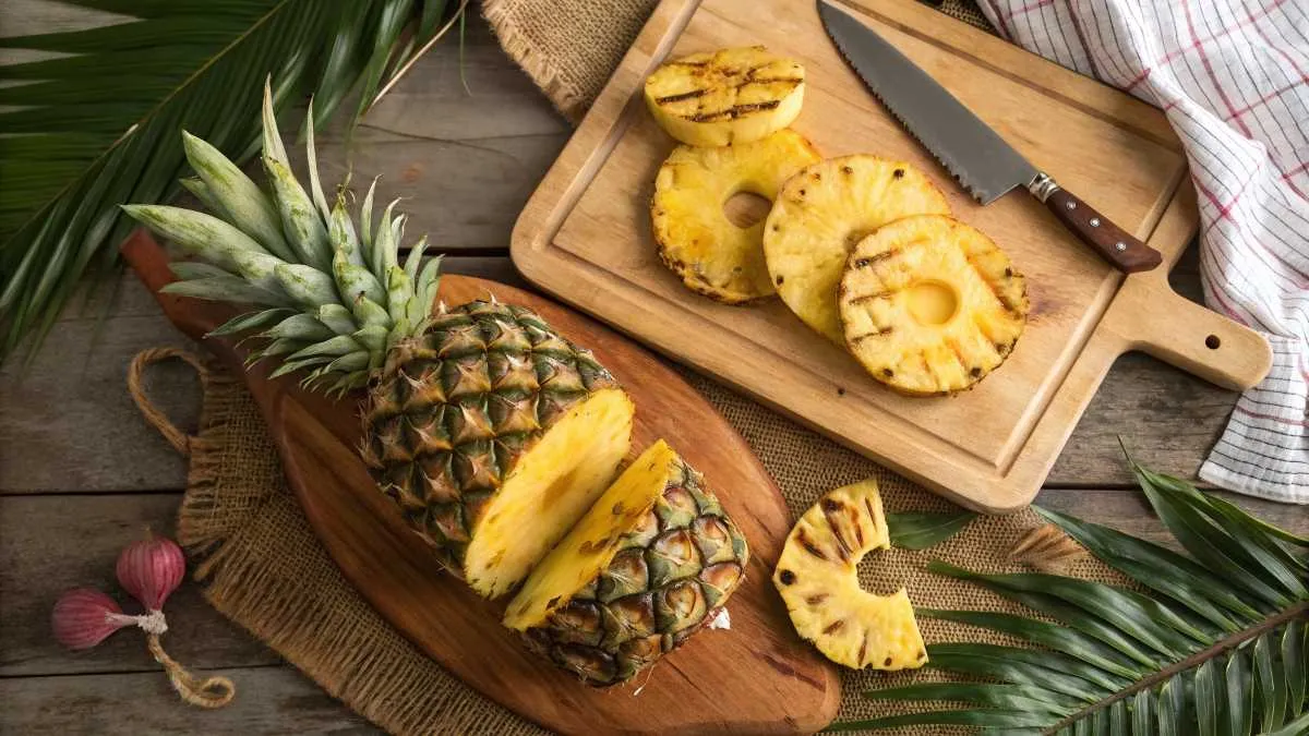 Whole pineapple, fresh slices, and grilled pineapple on a wooden table with tropical decor.