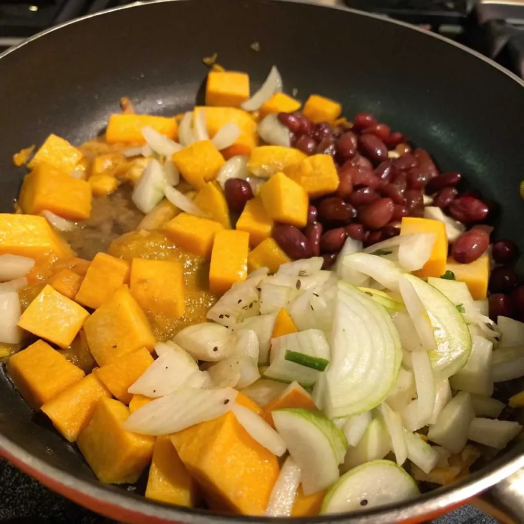 Chopped squash and sautéed onions and garlic in a skillet, part of the squash and kidney beans recipe preparation.