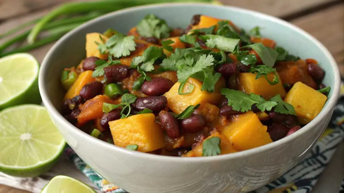 A completed squash and kidney beans dish, garnished with cilantro and lime, ready to serve.